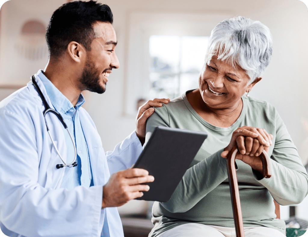 A doctor is holding a tablet computer, with one hand on the shoulder of an elderly patient. They are both smiling while looking at the test results.